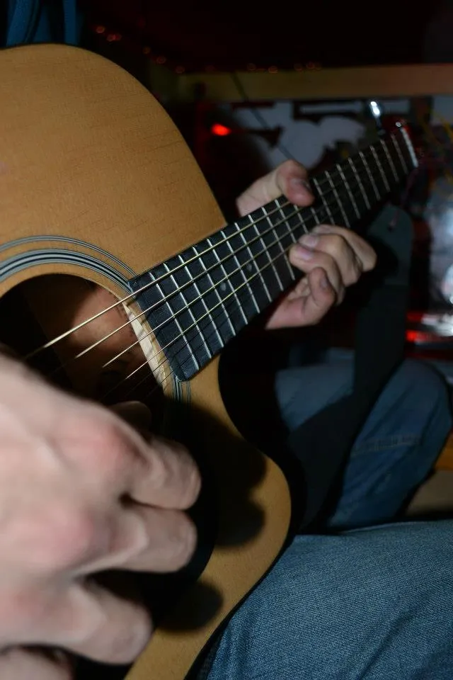 Hands on an acoustic guitar at an Open Mic session