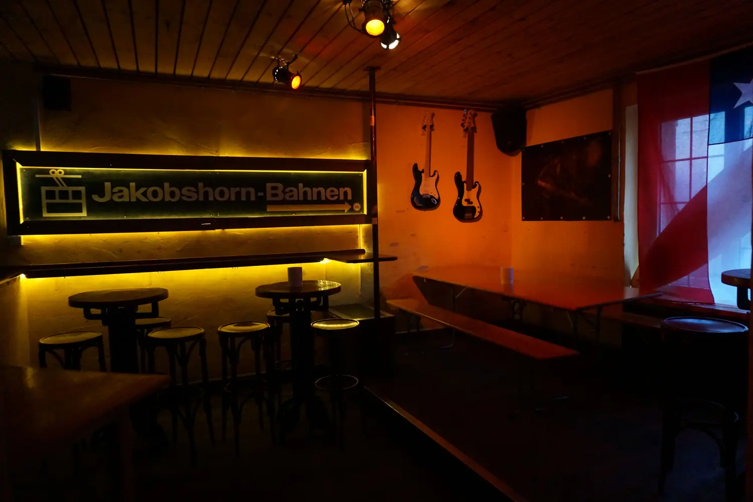 The empty room with the Jakobshorn cable car sign, high tables and two guitars on the wall